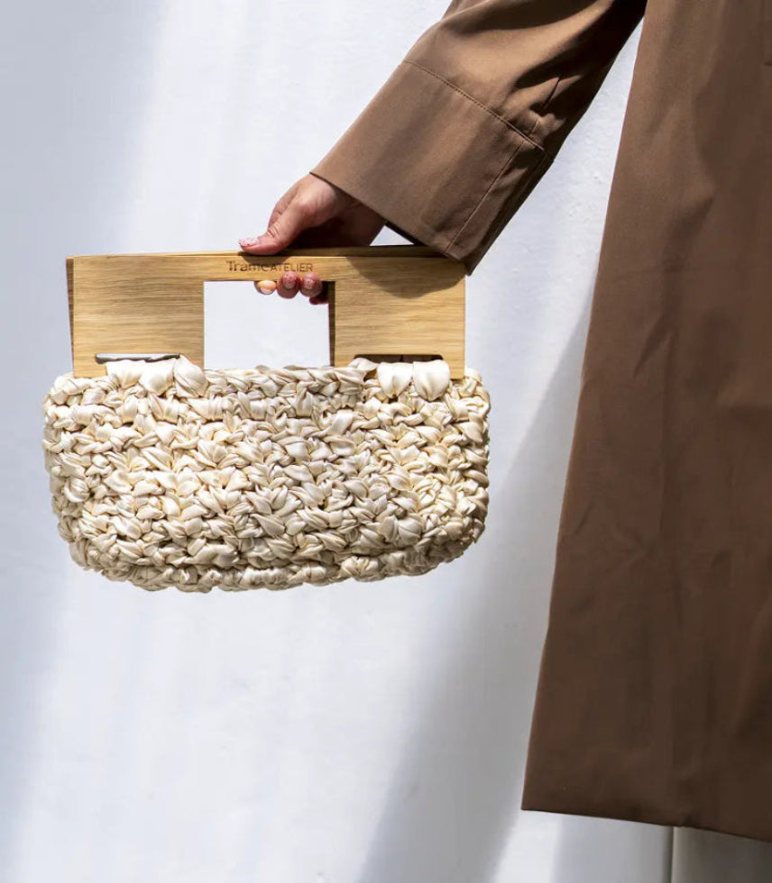 Person holding a textured handbag with wooden handle against a white background
